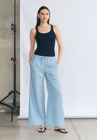 Granatowy top na ramiączkach w połączeniu z jasnoniebieskimi, szerokimi spodniami z elastycznym pasem i bocznymi kieszeniami. Czarne klapki dopełniają stylizację.