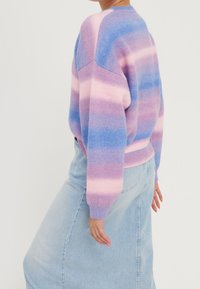 Lekki sweter z dzianiny z poziomymi paskami w kolorze różowym, fioletowym i niebieskim. Okrągły dekolt, długie rękawy i luźny krój. Połączony z dżinsową spódnicą.