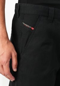 Black pants made of durable fabric feature a subtle sheen, visible stitching, and a small red and white label on the waistband.