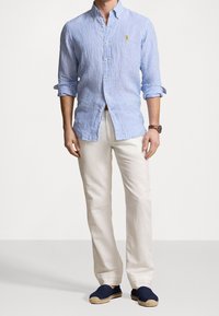 Světle modrá a bílá pruhovaná bavlněná košile s knoflíky, s ohrnutými rukávy, nošena s krémovými lněnými kalhotami a námořnickými espadrilkami.