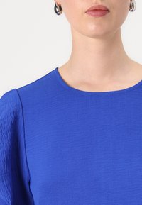 Royal blue textured top with a rounded neckline and short sleeves. Features a smooth fabric and minimal stitching detail.