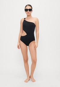 Maillot de bain une pièce noir avec un design asymétrique, un détail découpé sur le côté et une finition brillante. Accent de bretelle réglable.