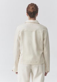 Světlý béžový denimový kabát s vypolstrovaným límcem, viditelným prošitím a manžetami na knoflíky, zobrazený ze zadní strany. Hladká textura.