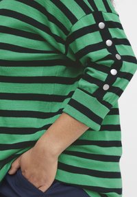 Zeleni in črni z žičnato pleteno jopico z gumbnimi detajli na rokavih, z ohlapnim krojem in rebrastimi manšetami.