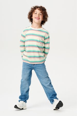 Gestreepte long-sleeve shirt in lichtgroen, blauw en rood, met een klein zakje en logo. Gecombineerd met blauwe jeans en witte sneakers.