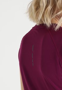 Kortärmad sporttröja i vinröd tyg, med en texturerad yta och reflekterande detaljer på baksidan, samt rund halsringning.