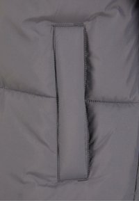 Grau isolierte Jackenstoff mit glatter Textur, ausgestattet mit einer Patten-Tasche und sichtbaren Nähten entlang der Nähte.