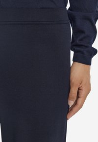 Marinblå träningstights med ribbad textur, elastisk midja och figurnära design. Handen vilar på sidan och visar detaljer.