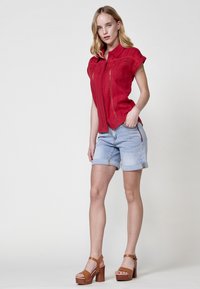 Rode shirt met korte mouwen heeft een kraag en decoratieve stiksels. Gecombineerd met lichtblauwe denim shorts en bruine plateau-sandalen.