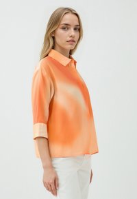 Orangenfarbige Gradient-Bluse mit einem Kragen, drei Viertelärmeln und leichtem Stoff. Abgerundeter Saum und glatte Textur.