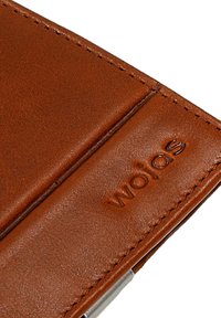 Brązowy skórzany portfel o gładkiej teksturze, z przeszytymi brzegami i wytłoczonym logo "wojas". Kompaktowy design z metalowym akcentem po boku.