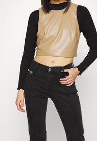 Avkortad, ljusbrun imitationlädertop med en slät textur; kombinerad med högmidjade svarta skinnyjeans med en dragkedjeficka.