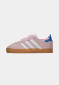 Shoe Adidas Gazelle em rosa com riscas brancas, sola de borracha e tab do calcanhar azul, vista lateral sobre fundo simples.