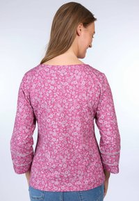 Magenta top with floral print, three-quarter sleeves, rounded neckline, and decorative stitching along sleeve hems.