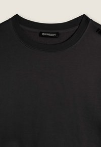 Camiseta de algodón negra con cuello redondo y mangas cortas. Presenta un acabado texturizado y el logo 'FREDDY' en el hombro.
