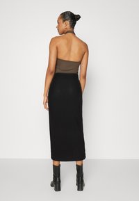Hnědý halter top v kombinaci s černou rýhovanou midi sukní. Černé kotníkové boty dotvářejí vzhled. Jednoduchý a přiléhavý design.