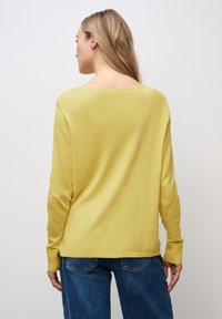 Langarm-Sweater mit Rundhalsausschnitt aus weichem, strukturiertem senfgelbem Stoff. Kombiniert mit blauen Jeans. Einfaches, lässiges Design.