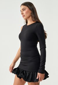 Black dress with a fitted bodice and a one-sleeve design, featuring a ruffled hemline made of satin-like material.