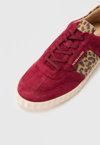 Red suede sneaker with a leopard print fabric accent, round toe, lace-up closure, and a textured cream rubber sole.