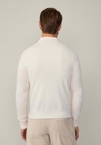 Bílý pletený svetr s vysokým límcem, žebrovanými manžetami a lemem. Hladký povrch s přiléhavým střihem, zobrazený zezadu.