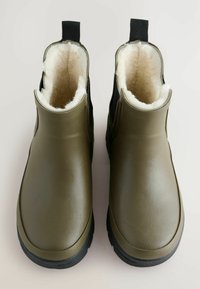 Olijfgroene waterdichte enkelboots van gestructureerd synthetisch materiaal, met een zachte crème binnenvoering en zwarte rubberen zolen.