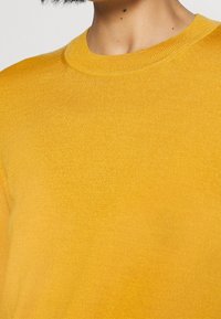 Maglione giallo in maglia con scollatura a girocollo a costine e texture liscia, che presenta un colore uniforme senza motivi o dettagli hardware.