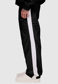 Melni sporta bikses ar baltu sānu strīpu, ar elastīgu jostasvietu un gludu tekstūru. Valkātas ar baltām kedām.