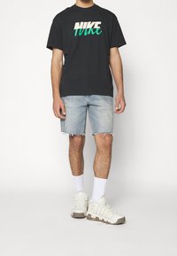 Černé bavlněné tričko s bílým a tyrkysovým logem Nike, světle modré zničené džíny šortky a bílé boty doplněné bílými ponožkami.