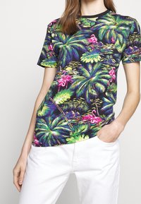 Krátký rukáv černé tričko s tropickým potiskem, na kterém jsou palmové listy a růžoví plameňáci. Vyrobeno z měkké látky s volným střihem.