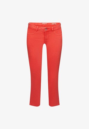 Jeans cortos color coral con aberturas laterales en el dobladillo, combinados con sandalias beige de tiras cruzadas. Se aprecia la textura del denim en los pantalones.