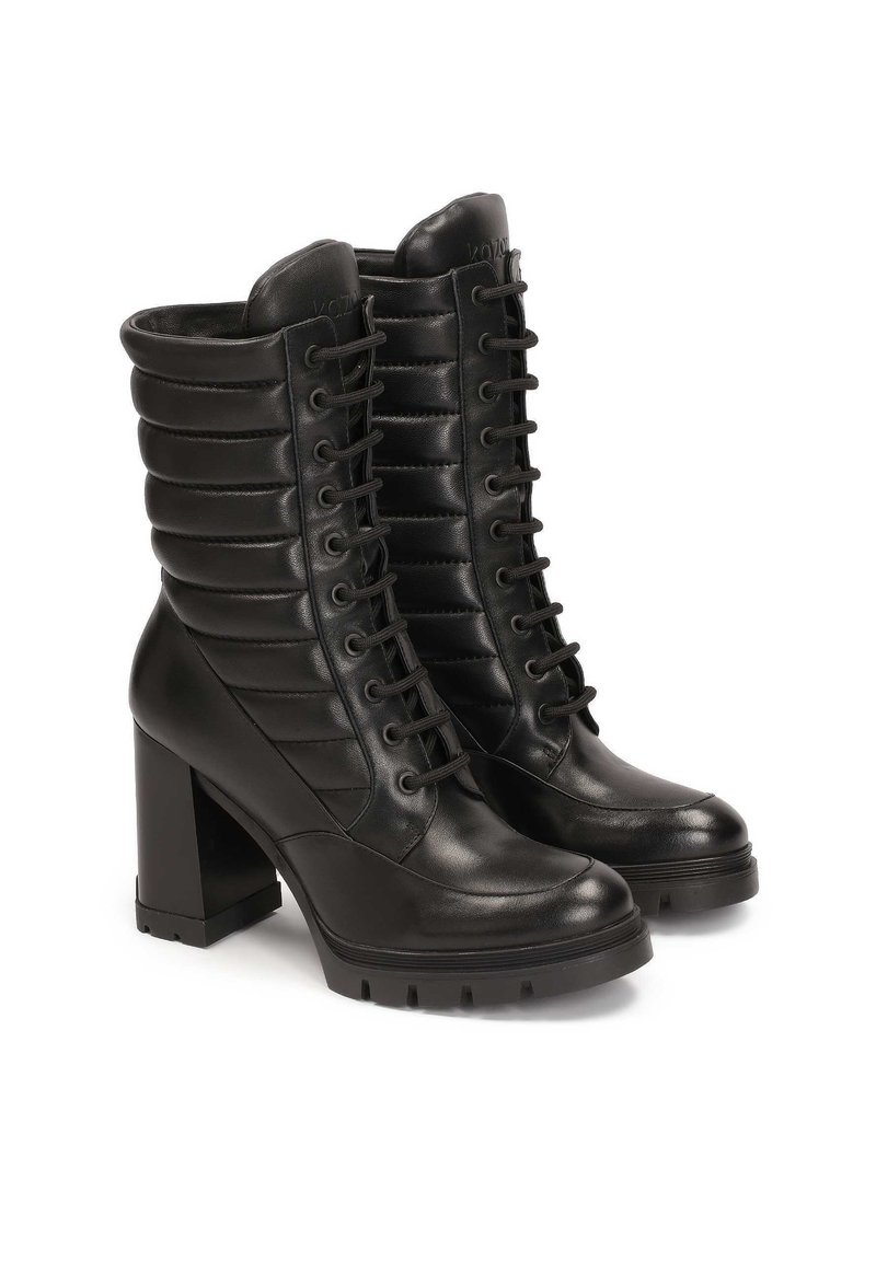 Botines de cuero negros con un tacón alto en bloque, detalles acolchados a lo largo del eje y cordones en la parte frontal. Suela robusta para mayor tracción.