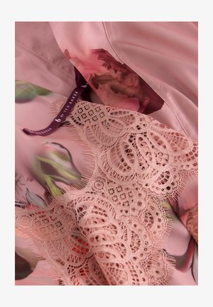 Vaaleanpunainen kukkakuvioitu kangas, jossa on monimutkainen pitsireunus. Pehmeä satiinipinta ja punotut yksityiskohdat lisäävät visuaalista viehätystä. Merkki näkyvissä.