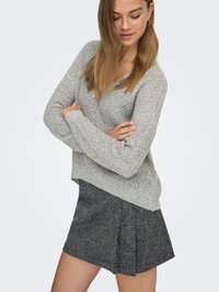 Sivi pleteni džemper širokog kroja s V-izrezom u kombinaciji s crnom plisiranom suknjom s teksturom. Ovaj outfit ističe rebraste detalje i opušten dizajn.