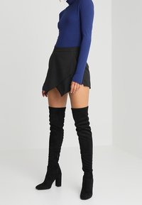 Blå långärmad topp, svart insvängd mini kjol och svarta höga stövlar med klack. Släta material med figursydda designer och ett lager-på-lager utseende.