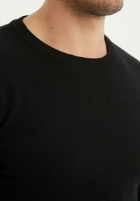 Pull noir en maille avec col rond, à la texture lisse et au col côtelé. Gros plan mettant en avant la qualité du tissu et la couleur.