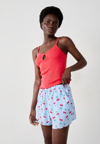 Rode mouwloze top met een sleutelgaatje-detail, gecombineerd met blauwe geruite shorts versierd met een kersenpatroon.