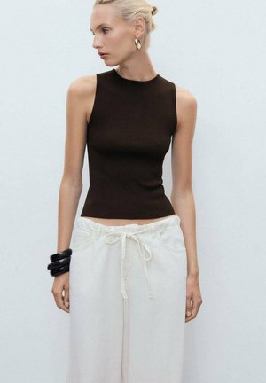 Haut sans manches brun au design ajusté, associé à un pantalon blanc ample avec taille à cordon. Les accessoires comprennent un bracelet noir.
