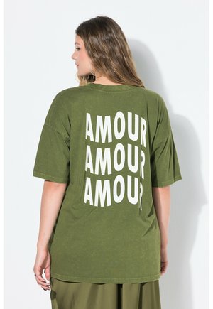 Olijfgroen oversized t-shirt van katoen met korte mouwen. Heeft grote witte tekst met de woorden "AMOUR" op de achterkant.