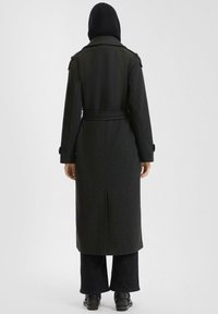 Zwarte wollen trenchcoat met een getailleerd ontwerp, een ceintuur in de taille en schouderepauletten. De achterkant heeft een centrale split en een gestructureerde stof.