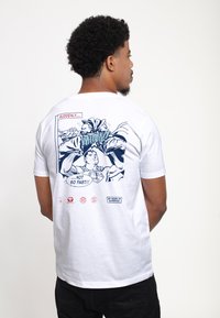 Hvid bomulds t-shirt med et blåt comic-style print på ryggen, der viser actionbilleder og teksten "PLUDSELIGT... IKKE SÅ HURTIGT!!"