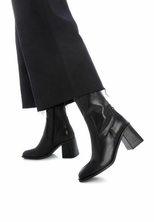 Botas de cuero negras hasta el tobillo con punta cuadrada y tacón de bloque, con cierre lateral y detalles de costura minimalistas.