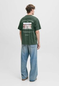 Roheline puuvillane t-särk, millel on graafikaprindiga ja tekstiga seljaosas. Ühendatud lodevate helesiniste teksadega. Lihtne ümmargune kaelus.