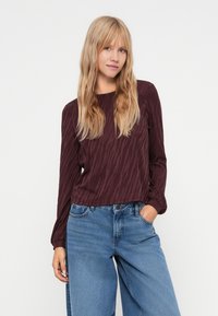 Bordeauxfarbenes Langarmoberteil mit dezentem Tigerstreifenmuster, aus weichem Stoff, runder Ausschnitt, kombiniert mit hochgeschnittenen blauen Jeans.