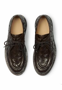 Tamnosmeđi pleteni kožni cipele s okruglim prstima, s ravnim potplatom i vezicama. Glatka textura s pletenim uzorkom preko površine.