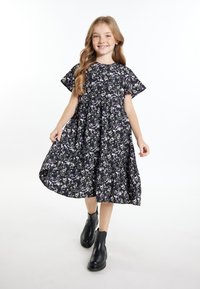 Zwart bloemenjurk met korte mouwen, voorzien van paarse en witte bloemen, geplooide taille en vloeiende rok. Gekozen in combinatie met zwarte enkellaarsjes.