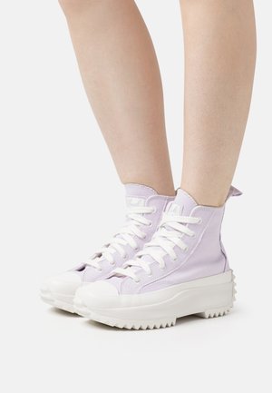 Zapatillas altas de lona púrpura claro con suelas de goma blanca. Las características incluyen puntera redonda, gruesa plataforma y cordones prominentes.