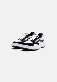 Sneaker bianco e nero con tomaia in suede e mesh, design zigzag prominente, lacci piatti e suola bianca chunky con dettagli testurizzati.