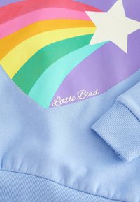 Felpa azzurra chiara con un design colorato a arco iris, caratterizzato da strisce rosse, rosa, arancioni, gialle, verdi e turchesi, e una stella bianca.
