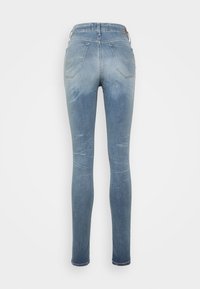 Jeans skinny azzurri chiari con tasche posteriori e dettagli di scoloritura leggeri, mostrati da dietro su uno sfondo bianco.