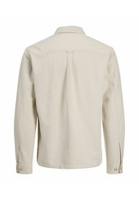 Hellbeiges Langarmhemd aus strukturiertem Stoff, mit geknöpften Manschetten, Rückenkoller-Detail und klassischem Kragen.